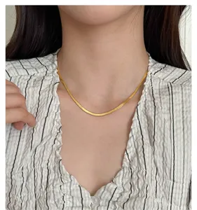 Close-up detail of a minimalist gold-plated flat snake bone chain necklace worn on neck.