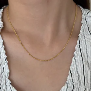 Close-up detail shot of a delicate thin gold chain necklace worn on the neck, elegant style.
