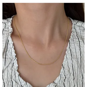 Detail shot of a minimalist gold plated snake chain necklace worn on the neck, elegant design.