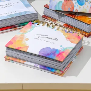 Close up of watercolor desktop calendar with gold spiral binding and inspirational cover.