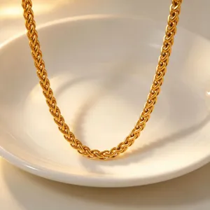 Close-up detail shot of a trendy gold woven chain necklace displayed on a white plate.