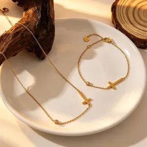 Detailed close-up of minimalist gold cross necklace and bracelet set on ceramic plate.
