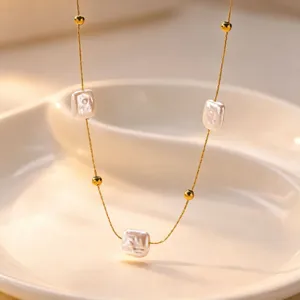 Delicate gold chain necklace with white square pearls, elegant detail close up view.