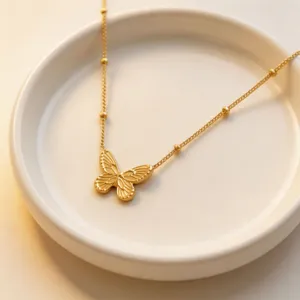 Detailed close-up view of a gold butterfly pendant necklace on white ceramic tray.