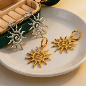 Detailed view of trendy spiral sun metal charm earrings in gold and silver finish on a plate.
