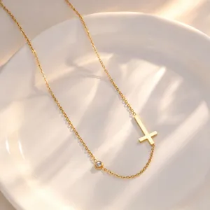 Minimalist stainless steel cross necklace with a single stone detail, elegant gold tone jewelry.