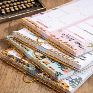 Detailed close-up view of weekly meal planner notebook with gold spiral binding on wooden table.