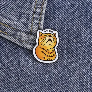 Close-up detail shot of a funny screaming orange cat enamel pin with AWOO text on denim.