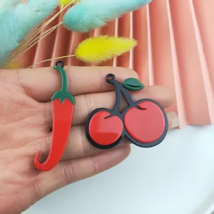Primer plano de bonitos dijes acrílicos rojos de cereza y chile para pendientes DIY.
