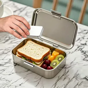 Stainless steel bento lunch box detail view showing metal finish, sandwich, and fresh fruits.