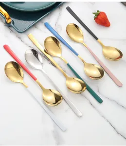 Primer plano de cucharas de acero inoxidable con mangos de colores y cabezales dorados, ordenadas.