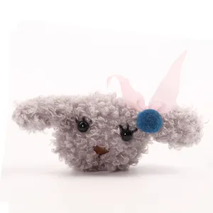 Gedetailleerd uitzicht op grijs pluche puppy pop broche met roze strik en blauwe pompon.