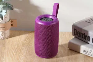 Tragbarer zylindrischer Bluetooth-Lautsprecher mit Stoffgewebe und praktischem lila Tragegurt.