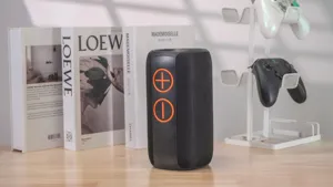Detailed view of black wireless bluetooth speaker with orange volume buttons on wooden table.