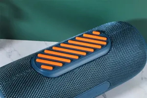 Haut-parleur Bluetooth cylindrique portable avec maille en tissu et boutons orange vibrants.