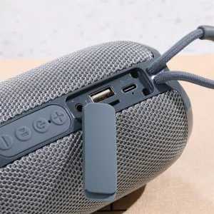 Primer plano detallado del altavoz Bluetooth cilíndrico portátil en malla gris con puertos.