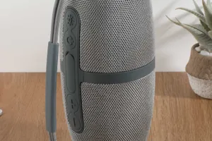 Portable wireless bluetooth speaker with gray fabric mesh and convenient carrying strap.