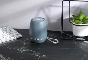 Mini altoparlante Bluetooth portatile grigio con cordino e pulsanti di controllo.