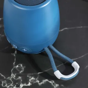 Dettaglio mini altoparlante Bluetooth portatile blu con scocca e cordino in tessuto.