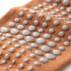 Close-up detail of anti-slip yoga socks with grey silicone dots on brown knitted fabric.