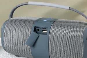 Gros plan de l'enceinte Bluetooth portable avec tissu maillé, boutons et fentes de connexion.