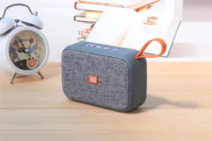 Portable wireless bluetooth speaker with fabric mesh and orange strap, compact stereo design.