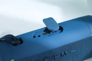 Portable wireless blue bluetooth speaker with fabric mesh design and audio interface detail.