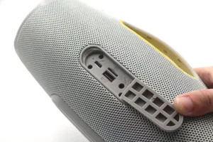 Portable bluetooth speaker detail view, grey fabric mesh exterior with rubber port flap cover.