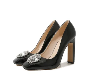 Close-up detail of black patent leather high heels featuring a sparkling rhinestone buckle.
