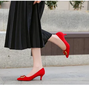 Detalle de zapatos de tacón rojo con punta afilada, tacón sensato y hebilla metálica dorada llamativa.