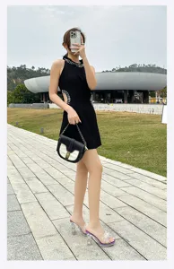 Detail view of clear crystal chunky heel high heel mules worn outdoors with black dress.