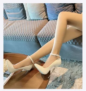 Close-up detail of white patent leather high heels with metal stiletto heel and ankle strap.