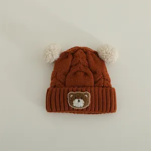 Cute bear patch detail of baby knit hat, fluffy pom poms, warm winter earflap beanie detail