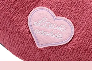 Close-up detail of stylish women's beret hat fabric texture with cute embroidered heart patch.