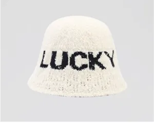 Vista detallada de un sombrero de cubo de felpa en crema con letras de la suerte negras.