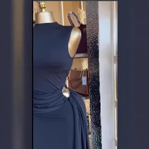 Vista detallada del elegante vestido largo negro sin mangas con hebilla metálica y drapeado lateral.