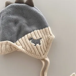 Dettaglio del berretto da neonato in maglia con punte di dinosauro, copriorecchie e bel ricamo.