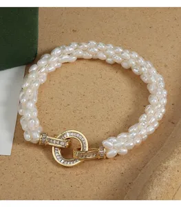 Nahaufnahme des mehrsträngigen Reis-Süßwasserperlenarmbands mit glänzendem Gold-Strassverschluss.