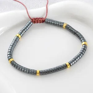 Bracciale in pietra ematite con distanziatori dorati e corda intrecciata rossa regolabile.