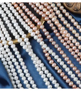Primo piano dettagliato di fili di perle d'acqua dolce naturali lisce bianche e rosa su seta blu.