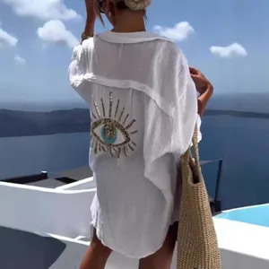 Detail view of the white beach cover-up shirt featuring sequin evil eye embroidery on the back.