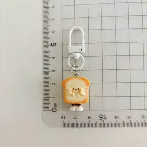 Cute toast bread keychain charm detail view clearly showing size on measurement grid ruler.