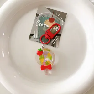 Detailed shot of transparent rainbow lollipop keychain with red bow and strawberry charm.