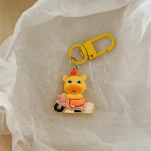 Close-up detail of a cute yellow cartoon animal keychain pendant riding a pink scooter accessory.