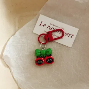 Close-up of cute black cat apple keychain pendant with green bow and red lobster clasp.