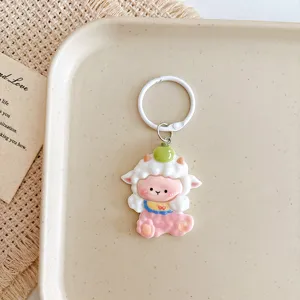 Close-up detail of a cute cartoon sheep keychain pendant with white ring and pink design.