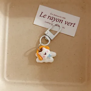 Detailed shot of the cute white puppy keychain pendant with yellow headphones and blue bow.