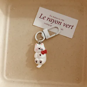 Cute white dog keychain pendant detail closeup showing glossy finish and red bow decoration.