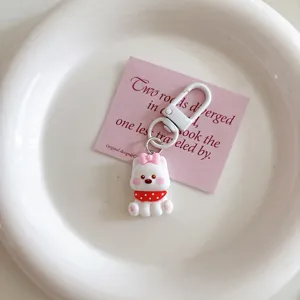 Close-up detail of a cute white puppy keychain with pink bow and red scarf inside a white dish.