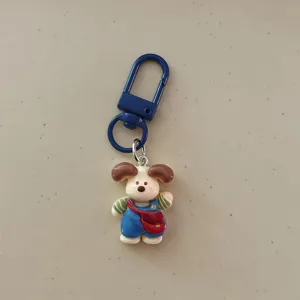Cute cartoon dog keychain with blue overalls and red bag, ideal detail charm for bags and keys.